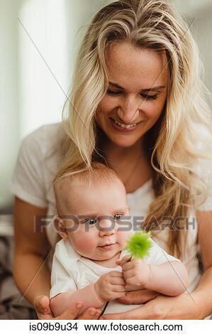 Baby girl sitting on mother's lap looking at flower View Large Photo Image Picture - Baby girl sitting on mother's lap looking at flower. Fotosearch