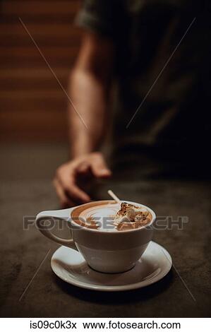Stock Photo - Barista at cafe counter with cup of mocha topped with toasted marshmallow, cropped shallow focus. Fotosearch