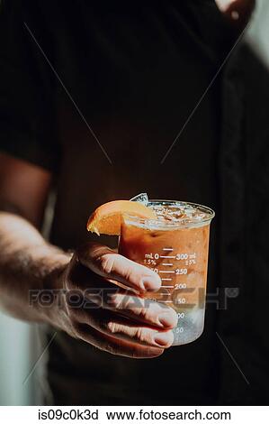 Stock Image - Barista holding fresh iced fruit juice in measuring jug, cropped close up of hand. Fotosearch
