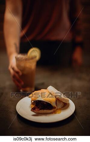 Barista placing iced drink by fried egg muffin on cafe counter, cropped low key View Large Photo Image Stock Image - Barista placing iced drink by fried egg muffin on cafe counter, cropped low key. Fotosearch