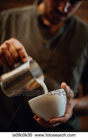 Stock Image - Barista pouring milk into coffee cup in cafe, cropped shallow focus. Fotosearch