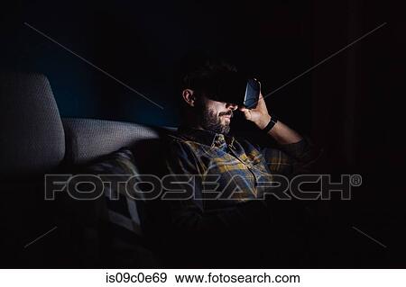 Bearded mid adult man sitting on sofa in darkness looking down through virtual reality headset View Large Photo Image Stock Photo - Bearded mid adult man sitting on sofa in darkness looking down through virtual reality headset. Fotosearch