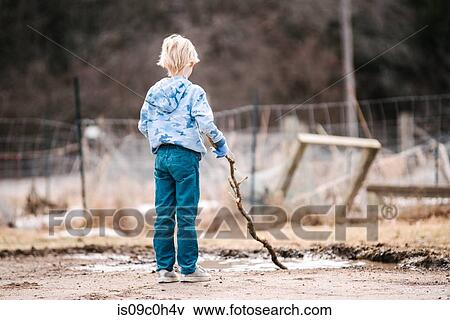 Blond boy on wasteland playing with tree branch in puddle, rear view View Large Photo Image Stock Photo - Blond boy on wasteland playing with tree branch in puddle, rear view. Fotosearch
