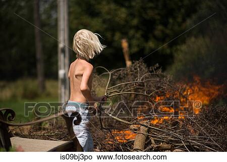 Blond haired boy placing tree branch onto garden bonfire View Large Photo Image Picture - Blond haired boy placing tree branch onto garden bonfire. Fotosearch