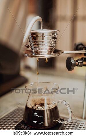 Stock Photography - Boiled kettle water pouring into coffee filter and dripping into jug on cafe counter, close up shallow focus. Fotosearch