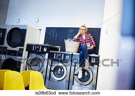 Bored woman sitting on top of washing machine at laundrette View Large Photo Image Stock Image - Bored woman sitting on top of washing machine at laundrette. Fotosearch