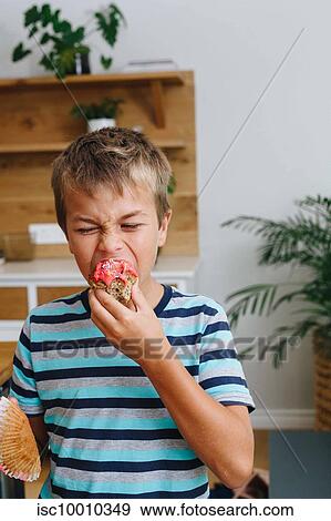 Boy biting into cupcake at home View Large Photo Image Stock Photo - Boy biting into cupcake at home. Fotosearch