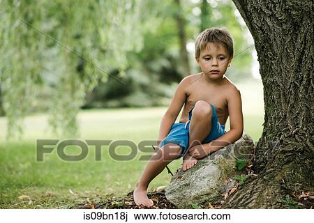 Stock Image - Boy daydreaming by tree trunk. Fotosearch