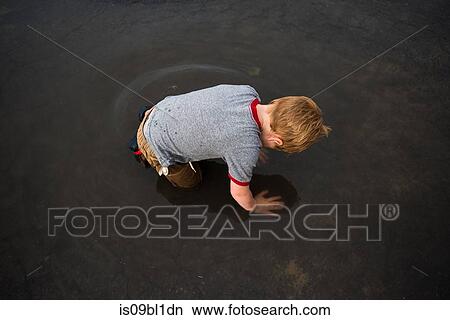 Boy kneeling in puddle on road View Large Photo Image Picture - Boy kneeling in puddle on road. Fotosearch