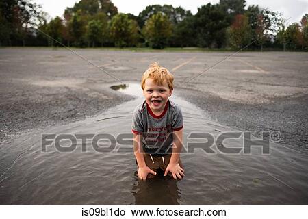 Boy kneeling in puddle on road View Large Photo Image Picture - Boy kneeling in puddle on road. Fotosearch