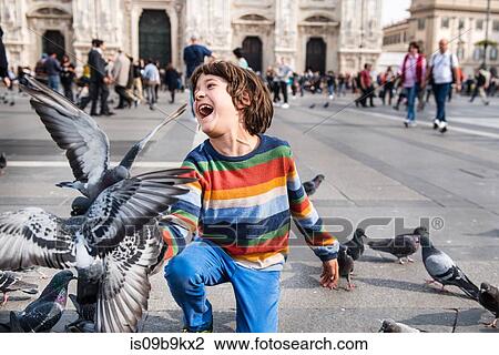 Boy laughing while feeding pigeons in square, Milan, Lombardy, Italy View Large Photo Image Stock Image - Boy laughing while feeding pigeons in square, Milan, Lombardy, Italy. Fotosearch