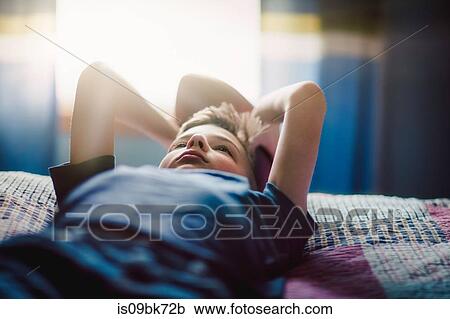 Stock Image - Boy on bed with american football. Fotosearch