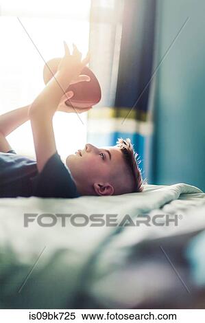 Stock Photography - Boy on bed with american football. Fotosearch