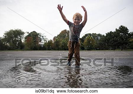 Stock Photography - Boy playing in puddle on road. Fotosearch