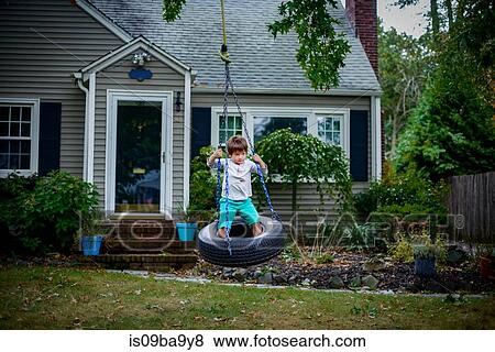 Boy playing on tyre swing in garden View Large Photo Image Stock Photo - Boy playing on tyre swing in garden. Fotosearch