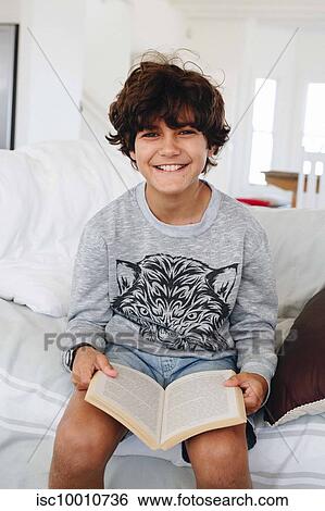 Stock Photograph - Boy reading book on sofa at home. Fotosearch