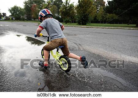 Stock Image - Boy riding bicycle on wet road. Fotosearch