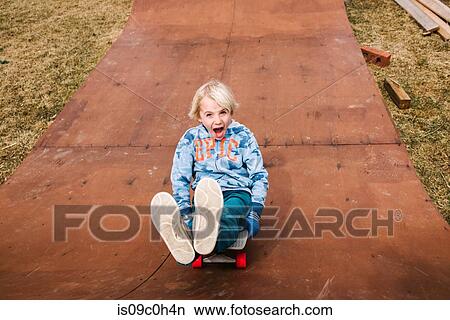 Boy sitting and skateboarding backwards down wooden skateboard ramp, portrait View Large Photo Image Picture - Boy sitting and skateboarding backwards down wooden skateboard ramp, portrait. Fotosearch