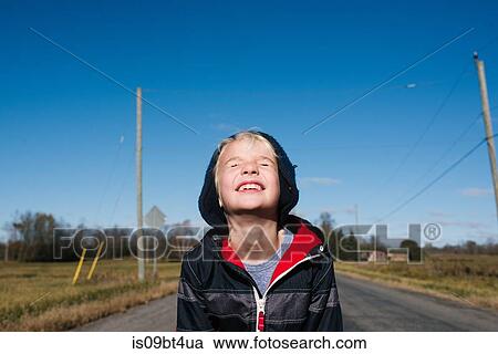 Stock Image - Boy squinting against clear blue sky. Fotosearch