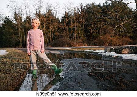 Stock Image - Boy standing ankle deep in rural meltwater puddle, portrait. Fotosearch