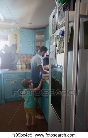 Stock Photography - Boy standing behind father at kitchen counter. Fotosearch