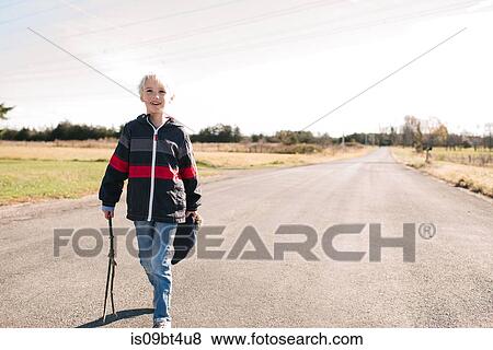 Stock Photo - Boy walking with stick on country road. Fotosearch