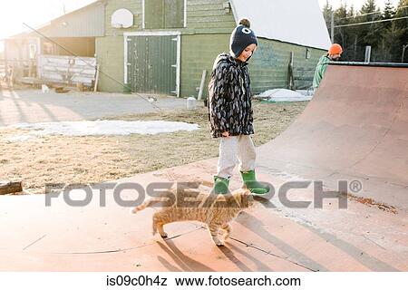 Stock Photo - Boy with cat looking at farmyard skateboard ramp. Fotosearch