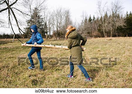 Brother and sister carrying log in field View Large Photo Image Stock Photo - Brother and sister carrying log in field. Fotosearch
