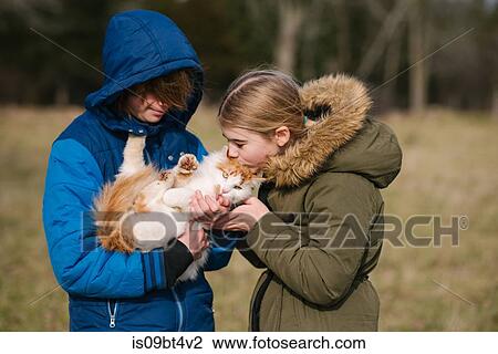Stock Image - Brother and sister cuddling cat in field. Fotosearch
