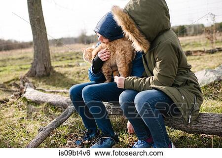 Stock Photograph - Brother and sister cuddling cat in field. Fotosearch