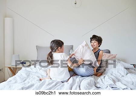 Stock Image - Brother and sister having pillow fight on bed. Fotosearch