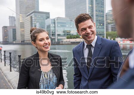 Stock Image - Businessman and businesswoman in discussion outdoors, Canary Wharf, London, UK. Fotosearch