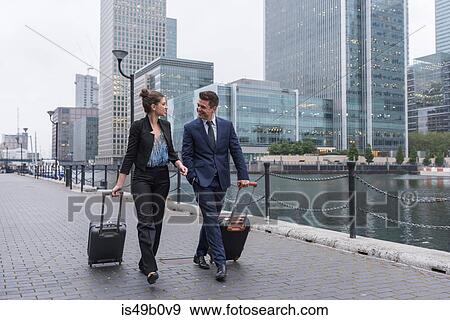 Stock Photo - Businessman and businesswoman pulling trolley luggage, Canary Wharf, London, UK. Fotosearch