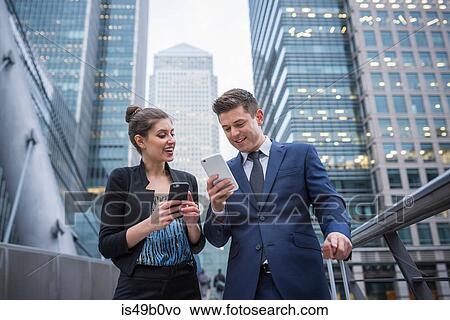 Picture - Businessman and businesswoman using mobile phone, Canary Wharf, London, UK. Fotosearch