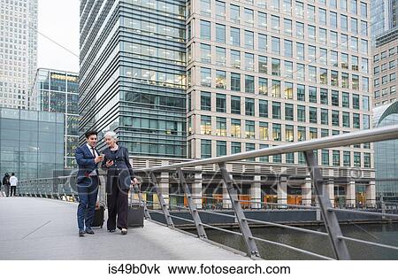 Businessman and businesswoman using mobile phone and pulling trolley luggage, Canary Wharf, London, UK View Large Photo Image Stock Image - Businessman and businesswoman using mobile phone and pulling trolley luggage, Canary Wharf, London, UK. Fotosearch