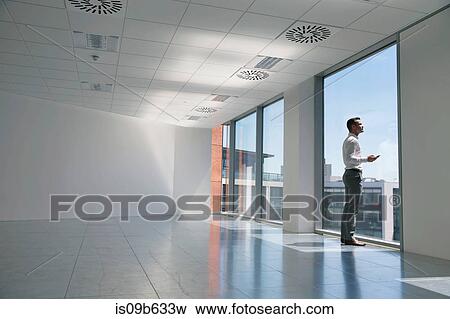 Businessman looking out of window, in empty office space View Large Photo Image Stock Photo - Businessman looking out of window, in empty office space. Fotosearch
