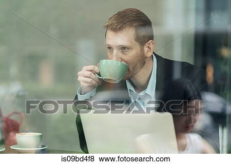 Stock Photo - Businessman sitting in cafe, drinking coffee, using laptop, viewed through window. Fotosearch