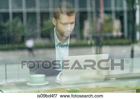 Businessman sitting in cafe, using laptop, viewed through window View Large Photo Image Stock Photo - Businessman sitting in cafe, using laptop, viewed through window. Fotosearch