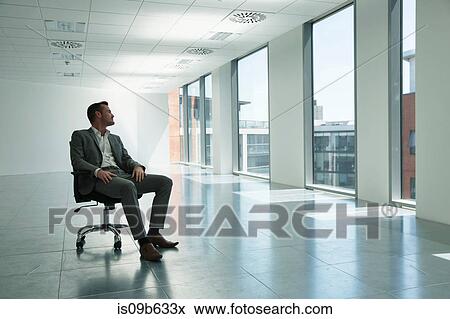 Businessman sitting in chair in empty office space, looking out of window View Large Photo Image Stock Photo - Businessman sitting in chair in empty office space, looking out of window. Fotosearch