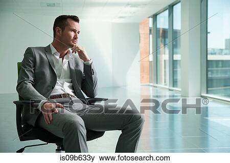 Businessman sitting in chair in empty office space, thoughtful expression View Large Photo Image Stock Photo - Businessman sitting in chair in empty office space, thoughtful expression. Fotosearch