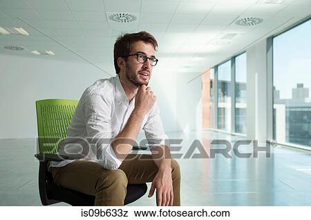 Stock Photo - Businessman sitting in chair in empty office space, thoughtful expression. Fotosearch