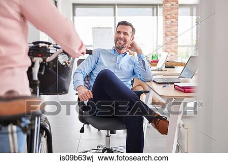 Businessman sitting in office chair smiling at colleague View Large Photo Image Stock Image - Businessman sitting in office chair smiling at colleague. Fotosearch