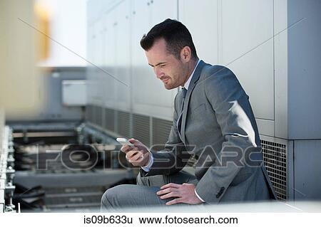 Businessman sitting outdoors, looking at smartphone View Large Photo Image Stock Photograph - Businessman sitting outdoors, looking at smartphone. Fotosearch