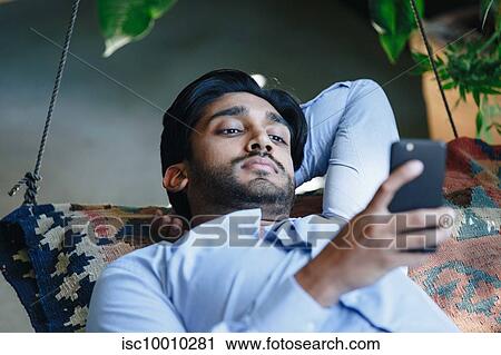 Stock Image - Businessman using cellular phone on swing. Fotosearch