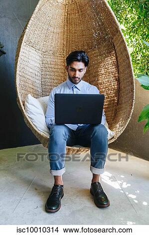 Businessman using laptop on cane swing chair View Large Photo Image Picture - Businessman using laptop on cane swing chair. Fotosearch