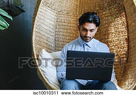 Businessman using laptop on cane swing chair View Large Photo Image Stock Image - Businessman using laptop on cane swing chair. Fotosearch