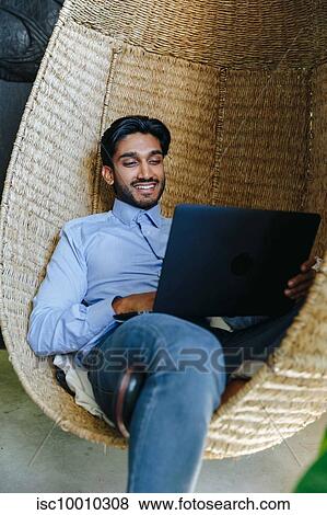 Stock Photo - Businessman using laptop on cane swing chair. Fotosearch