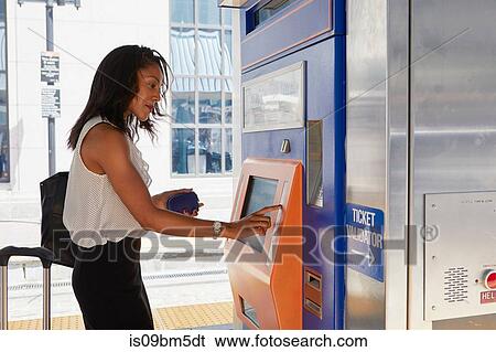 Stock Photograph - Businesswoman buying train ticket at machine. Fotosearch
