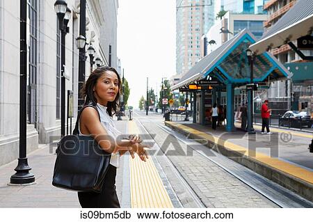 Stock Image - Businesswoman checking time by light rail line. Fotosearch