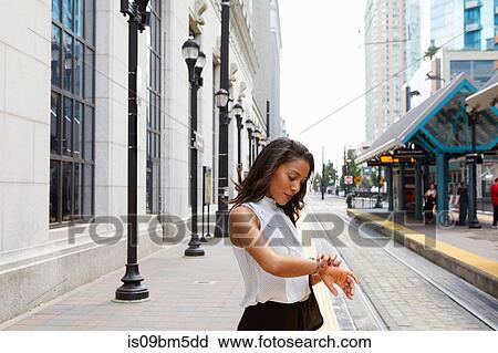Stock Image - Businesswoman checking time by light rail line. Fotosearch